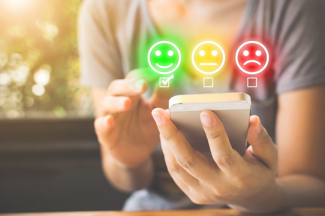 A person interacting with a smartphone screen displaying a digital customer satisfaction survey, with a glowing green smiley face icon actively selected.
