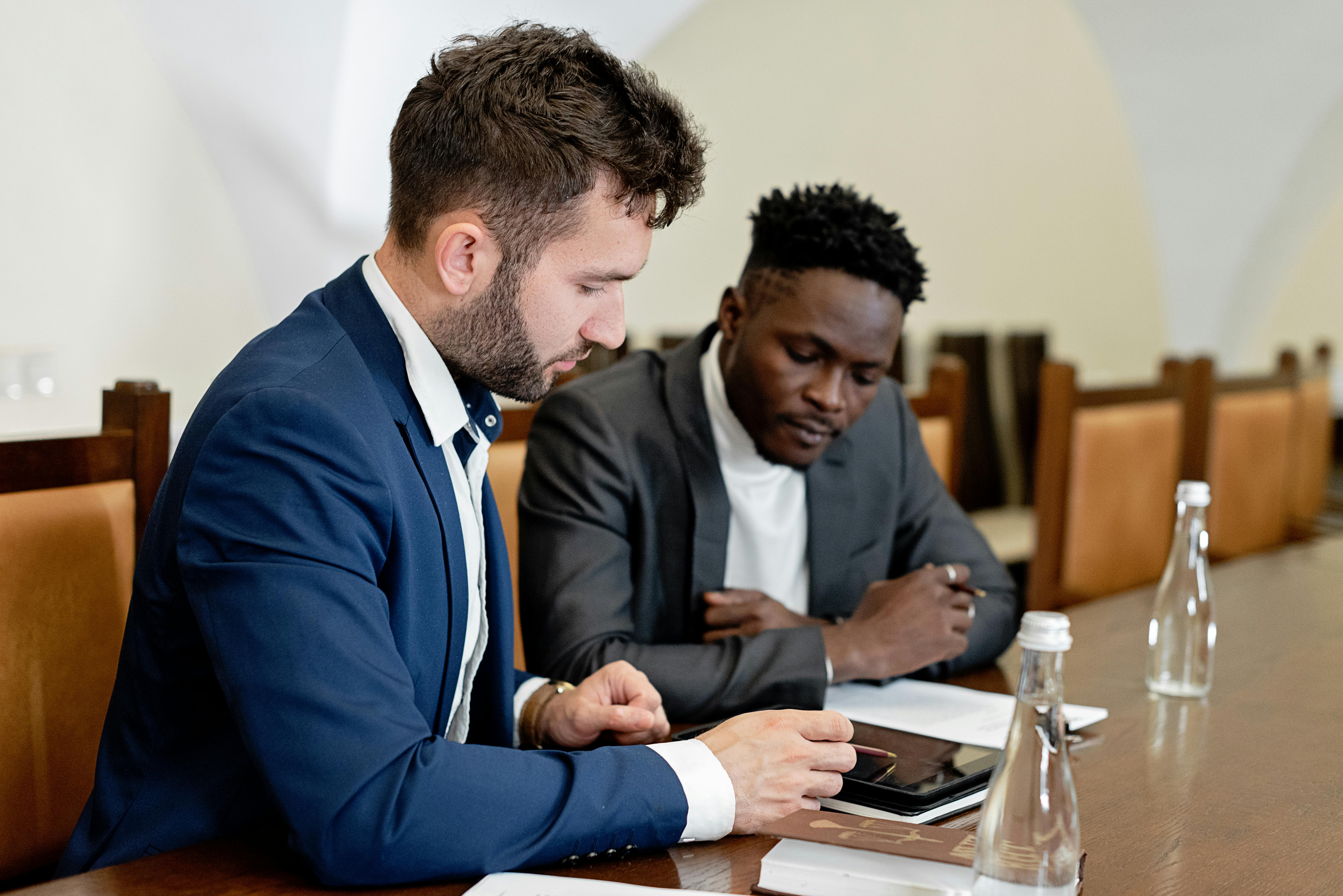 Two business professionals in suits sitting at a table, collaboratively analyzing information on a tablet device.